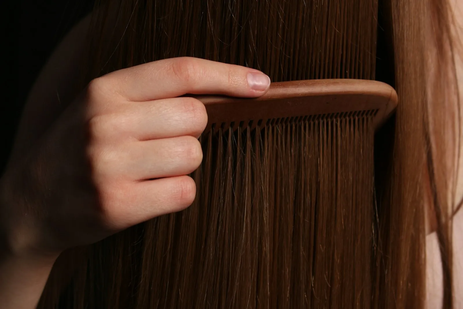 A hand combing long, smooth hair with a wooden comb
