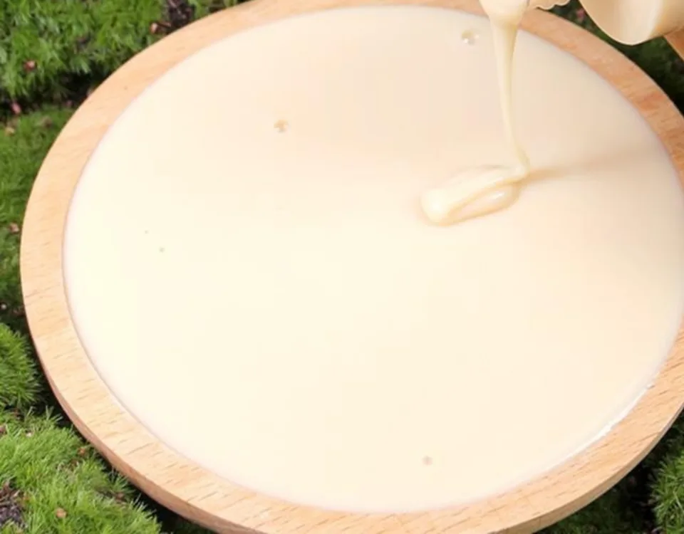 Creamy, pale shampoo being poured into a wooden bowl on a bed of moss